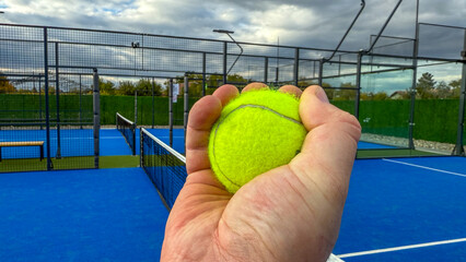 A hand grips a vibrant tennis ball on a cerulean padel court, evoking World Tennis Day and National...
