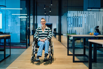 A confident smiling business woman in a wheelchair sitting in a bright modern office hallway,...