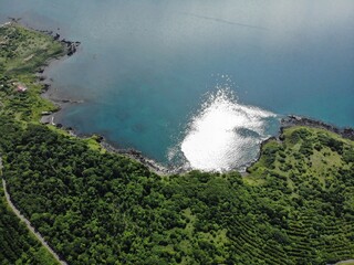 Aerial view of sunlit cove with turquoise water and lush green headland on Rishiri Island, Hokkaido, Japan, with rocky shoreline and coastal road