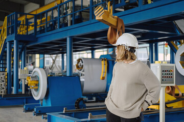 Industrial equipment for working with coil metal. Decoiler holds and unwinds metal coil. Slitting or cut-to-length line - cut coil metal into strips. Woman wearing helmet is working there.