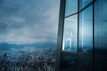 Successful businessman in suit standing in office looking through window at big city buildings