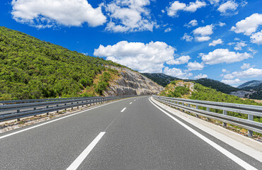 An empty, well-maintained asphalt road winding through a sunny, mountainous landscape