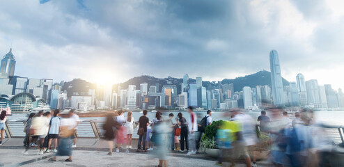 Tourists and citizens enjoying a cloudy day walking on the Hong Kong waterfront, with skyscrapers and victoria bay in the background