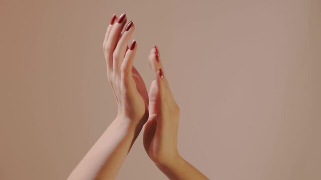 Closeup of elegant hands with glossy red manicure clapping in soft approving rhythm, palms meeting with gentle intent to convey admiration and recognition, tender tempo, polish and refined celebration