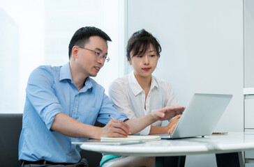 Obraz premium Two asian businesspeople working together in the office while using laptop