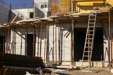 A concrete structure of a new residential building under construction, supported by temporary shoring props and scaffolding. Construction site with materials and a ladder.