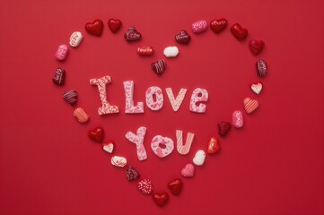 Heart-shaped candies forming a loving pattern on a crimson backdrop with multilingual expressions of affection