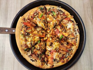 Delicious Super Supreme pizza with toppings of smoked beef, beef burger, smoked chicken, mozzarella cheese, mushrooms, pineapple, red peppers and green peppers put on a wooden table and ready to eat
