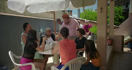 Lively group enjoying drinks and conversation around a table on a house terrace patio, creating a...