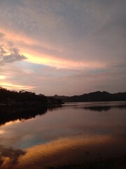 A beautiful sunset by the lake with a sky of orange and purple hues reflecting on the calm water. The peaceful and warm atmosphere captures nature’s tranquility, soothing both heart and mind.
