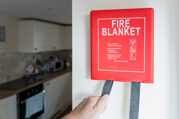 Newly installed Fire Blanket device seen being used for the first time by a home owner in a kitchen, due to a small fire whereby the flame will be smothered by the blanket. © Nick Beer