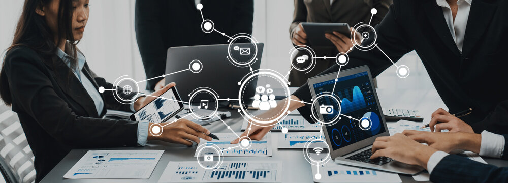 This image captures a dynamic business meeting where professionals collaborate using various devices and data analysis tools, emphasizing teamwork and modern communication. Amity