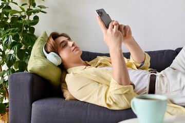 Young fashionable man relaxes on couch while enjoying music and checking his phone
