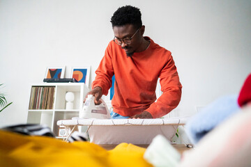Low angle of crop black male in casual clothing ironing t shirt while doing housework during weekend