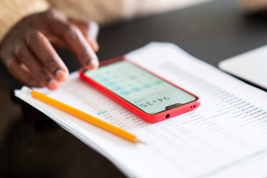 Crop anonymous black man using smartphone to check bills placed on table under pencil