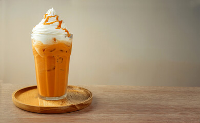  A glass of iced Thai tea blended with milk, topped with whipped cream and caramel sauce on pale gray wall background. Popular Thai drinks. copy space