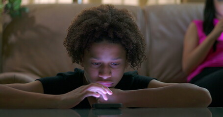 Close-up of boy focused on glowing smartphone screen, blank expression, emotional disconnection,...