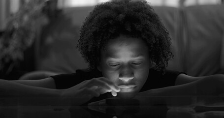Close-up of boy leaning on table, smartphone glow on face, blank expression, emphasizing digital...