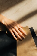 Manicured hand holding black and gold shopping bags on marble surface