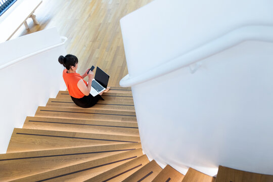 Woman sitting on staircase using smart phone and laptop