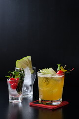Refreshing cocktails garnished with cherry and apple on black table
