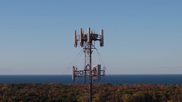 Telecommunication tower standing among autumn forest near a lake under clear blue sky