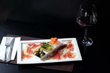 A delicious plate of carpaccio served with a glass of wine. The dish is beautifully presented on a rectangular plate, and the glass of wine sits beside it, creating a perfect pairing