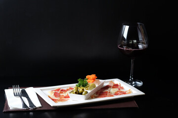 A culinary arrangement featuring a delicious dish and a glass of wine. The plate presents a beautifully arranged meat with a side dish, and next to it, a wine glass. 