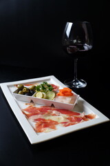 An exquisite culinary experience, a close-up of a plate with diverse appetizer and a glass of red wine. Featuring olives, vegetables and thin-sliced meat, a perfect combination for gourmet enjoyment