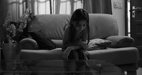 Young girl sitting on a couch leaning forward, introspective and isolated, showing signs of...