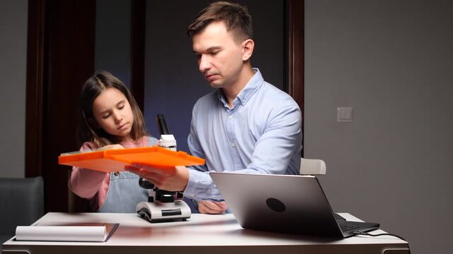 Father and daughter learning science with microscope and laptop