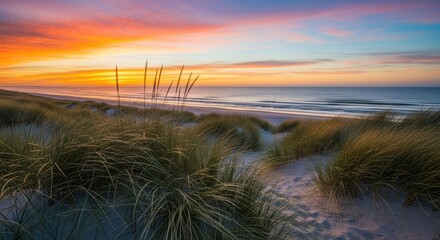 Stunning sunset paints the sky with vibrant oranges and purples over a serene ocean beach with windblown dunes and tall grasses.