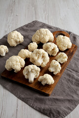 White Organic Raw Cauliflower Florets on a Wooden Board, side view.