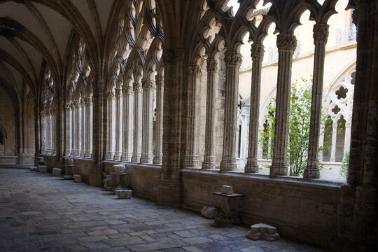 Ancient cloister corridor with gothic stone columns, vaulted ceiling and pointed arch windows in peaceful monastery courtyard