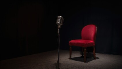 Single microphone positioned on a dimly lit stage beside a crimson seat