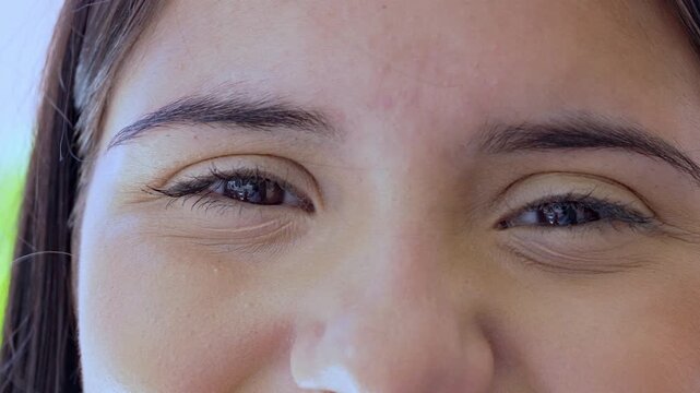 Close-Up Of Brown Eyes Girl Looking Forward With Slight Squint And Joyful Expression, Capturing Subtle Facial Detail And Emotional Depth In Natural Daylight