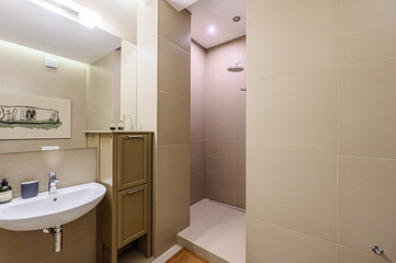 Clean, modern bathroom with beige tiles, a round sink, vanity, and a walk-in shower. Brightly lit and minimalistic design