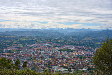 High angle view of densely built city center with residential neighborhoods framed by mountain landscape and cloudy horizon