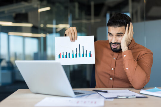 Stressed businessman on a video call showing a downward sales graph to colleagues, reacting to financial loss, bad news and disappointing quarterly results during remote work meeting