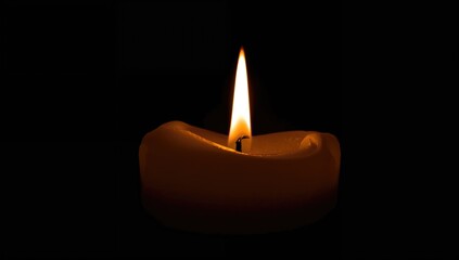 Detailed view of a glowing candle in pitch-black surroundings, with the flame lighting the candle's upper part.