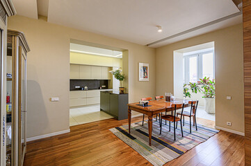 A cozy dining area flows into a modern kitchen with wood floors, a table, and a bright window