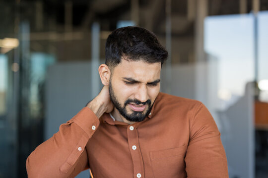 Young man experiencing discomfort and muscle tension in his neck and shoulder due to stress and long working hours, needing relief from chronic pain and discomfort