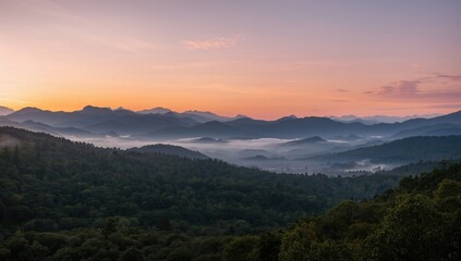 Fototapeta premium Panoramic view of dawn over mountain ranges with mist and golden hues, dense woodland in the foreground.