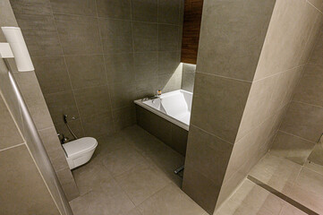Modern bathroom with gray tiles, white tub, and toilet. Clean, minimalist design