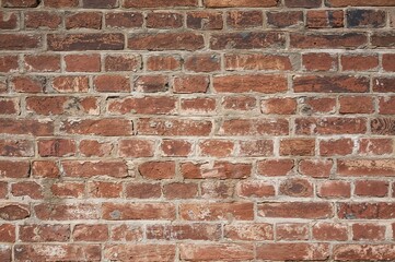 Fototapeta premium Close-up view of a weathered brick surface displaying a mix of colors and rough textures from long-term environmental wear, featuring visible fissures and repairs.