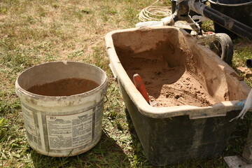 Side view of a container filled with mixed clay placed on the grass under a concrete mixer. A white...