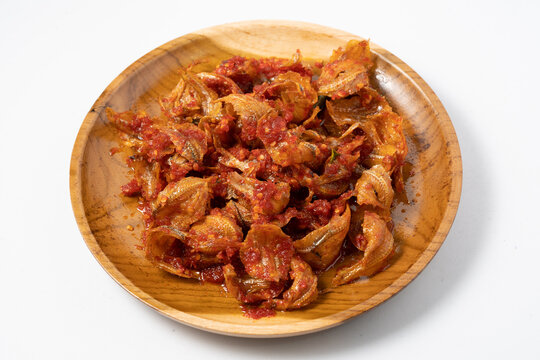 A top-down view of spicy salted fish, known as Ikan Asin kapas Balado, served on a round wooden plate. The small fish are coated in a red chili paste. Mojarra Salted Fish