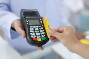 Close-up of customer making payment with credit card via POS terminal at pharmacy counter, representing digital payment, modern retail, contactless transaction and smart healthcare service.