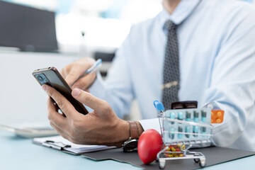 Close-up of businessman using smartphone with medicine pills in mini shopping cart, representing online pharmacy, e-commerce healthcare, digital health business and pharmaceutical marketing concept.
