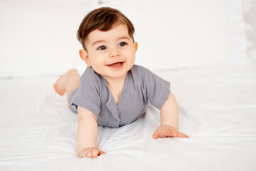 Fototapeta premium smiling baby on a white bed after sleeping, cute baby in a gray cotton bodysuit on a bed, space for text, baby boy